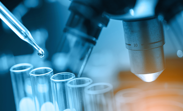 A pipette drops liquid into a series of test tubes. The lenses of a microscope are visible nearby.