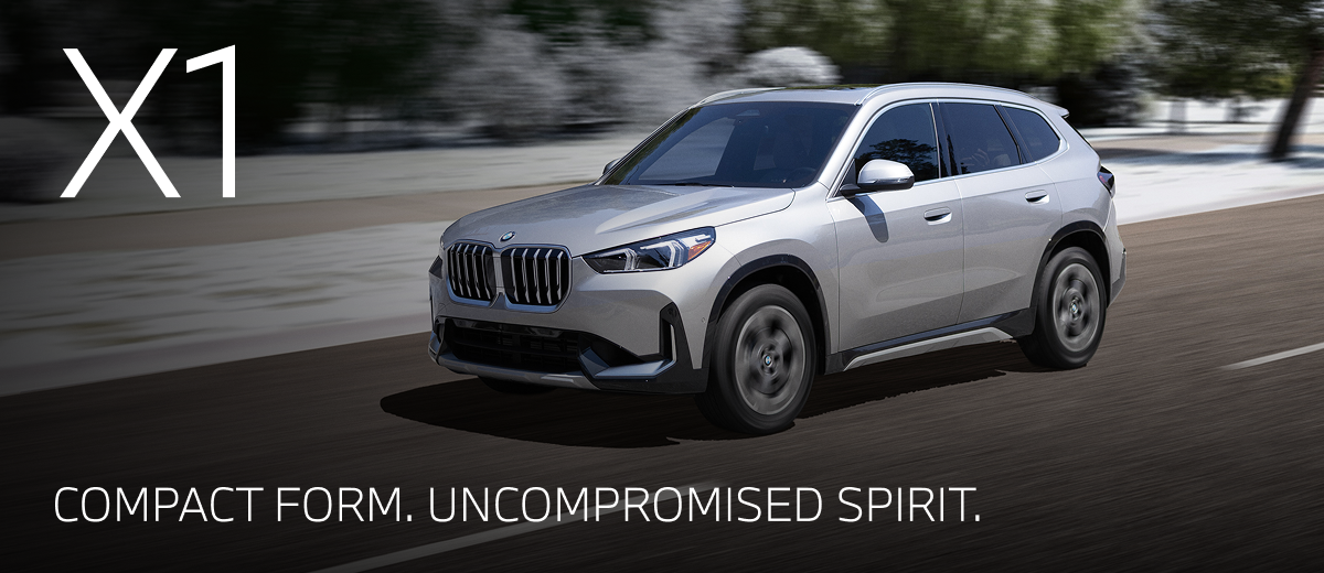 2026 BMW X1 driving down a winter road with snowy trees in the background