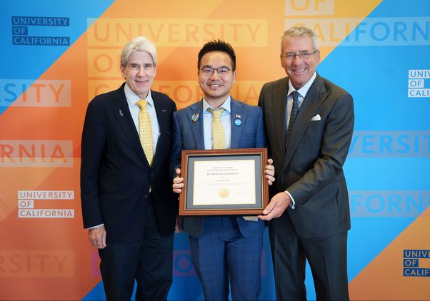 From left: Julio Frenk, Jack Feng and James B. Milliken in business attire, posing with a framed University of California award certificate against a blue-and-gold University of California backdrop, smiling for a presentation photo.