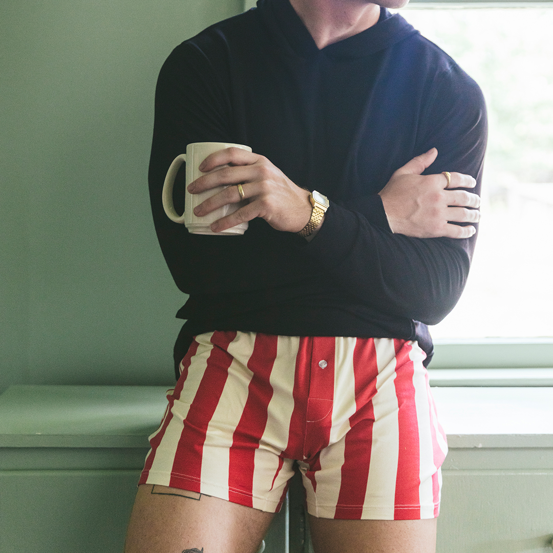 man standing in kitchen wearing black hoodie and red/cream stripe slim fit boxers