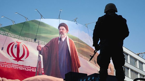 A member of the Iranian security forces stands guard under a large portrait of Iran's new Supreme Leader Mojtaba Khamenei.