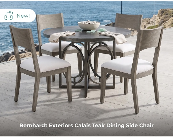 A round dark gray outdoor dining table paired with four matching wooden chairs with white cushions sits on a terrace overlooking the sea. Image Text: New! Bernhardt Exteriors Calais Teak Dining Side Chair
