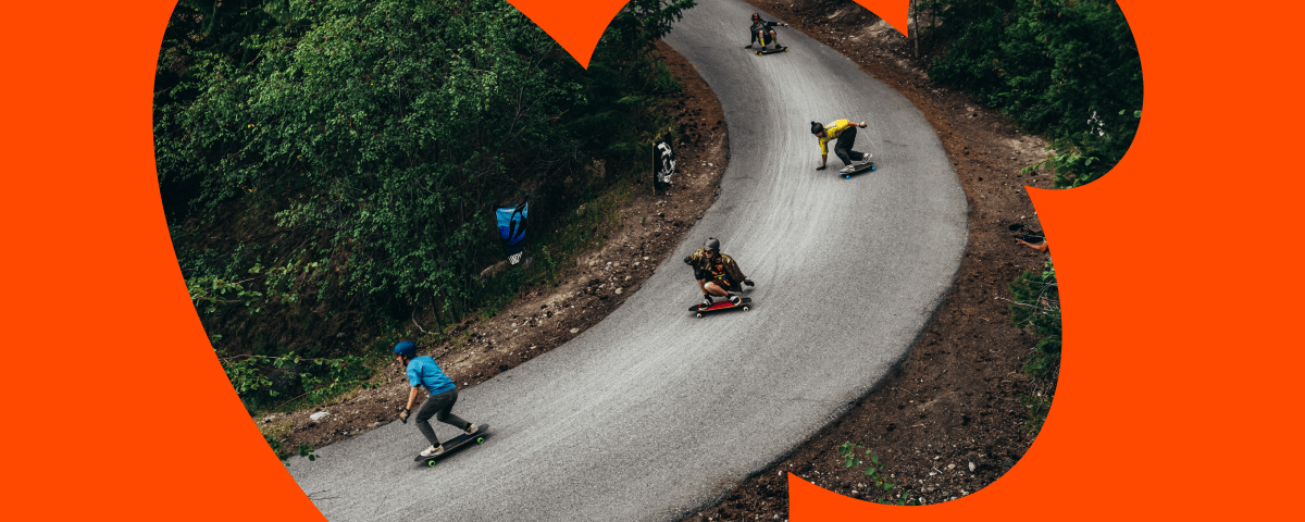 Multiple longboarders riding down a winding paved road through a forest, viewed through an orange circular arrow graphic mask.