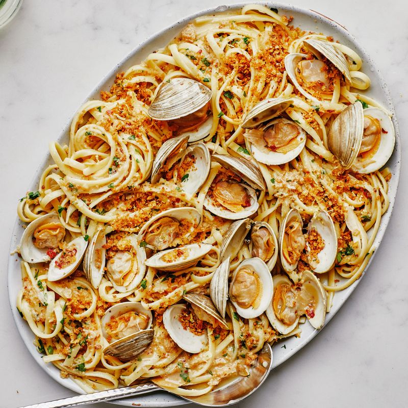 A large platter of linguine with clams alongside a bottle of white wine and two glasses.