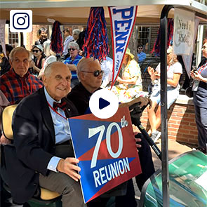 A Penn alumnus holding a 70th reunion poster while hitching a ride on a golf cart.