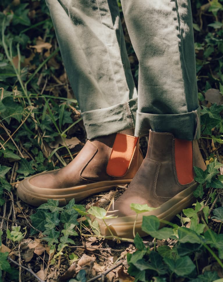 Guy standing in ivy wearing green pants and the beyond & back boot in elmwood/orange