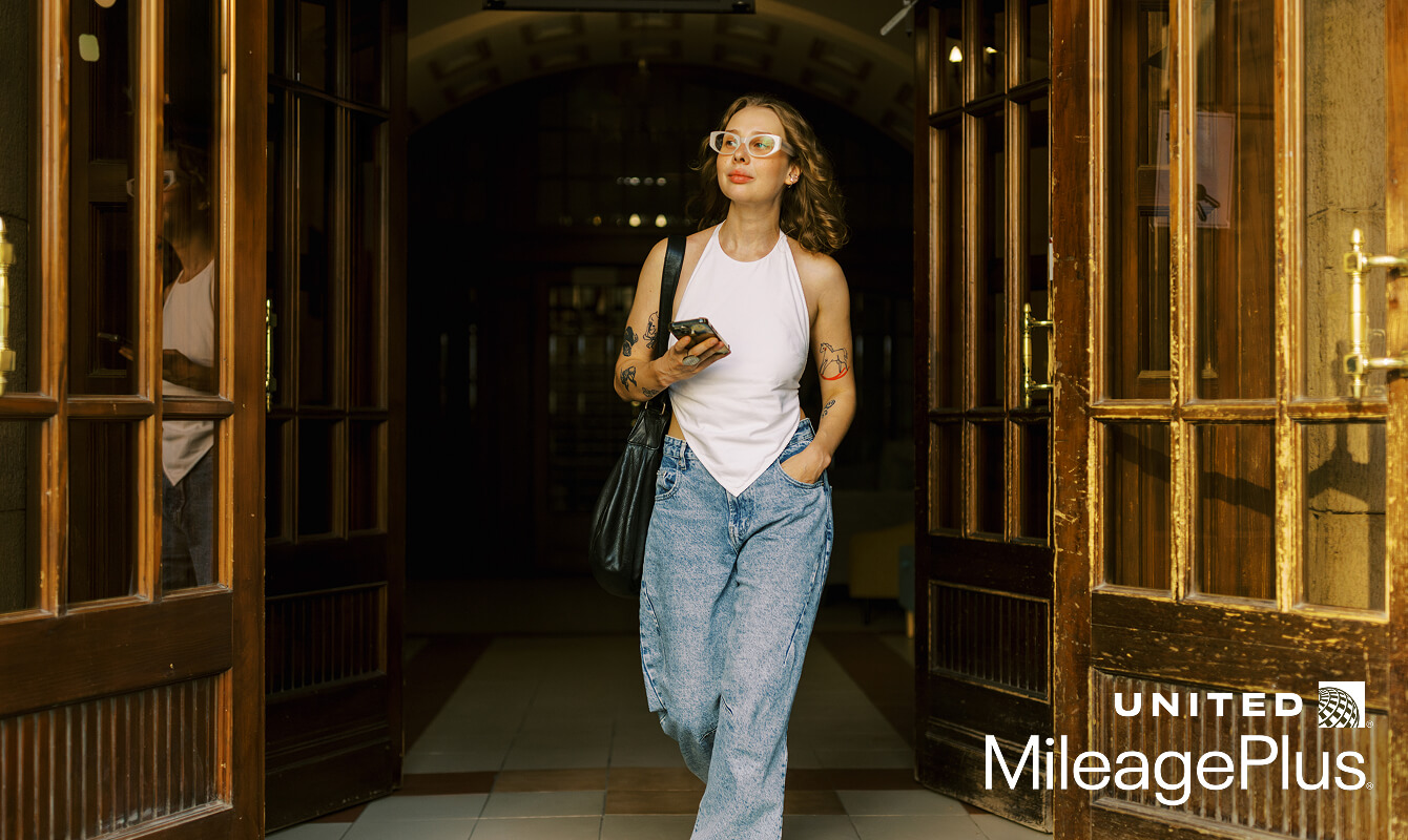 Woman walking outside at night holding her phone, wearing a white halter top and clear glasses.