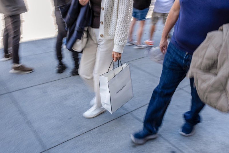 People walk carrying coats and shopping bags on a busy street.