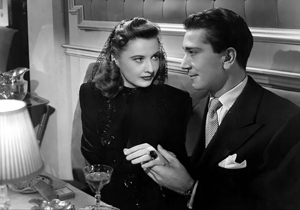 Black-and-white film still of a couple sitting next to each other at a restaurant holding hands