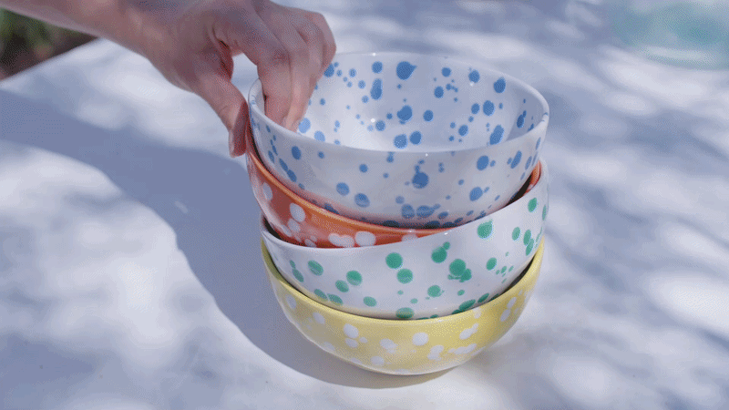 GIF with hand holding a stack of four Rafaela bowls in blue, orange, green and yellow with white splatter pattern