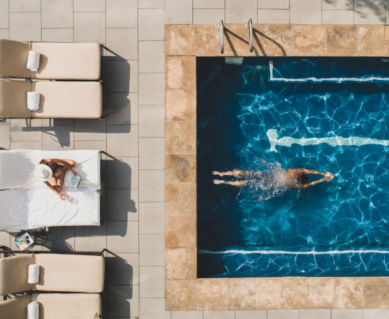 Aerial view of a swimmer in a pool beside sun loungers on a deck.