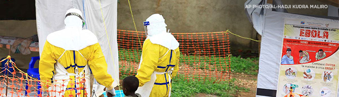 2 people in protective gear helping boy during Ebola outbreak.