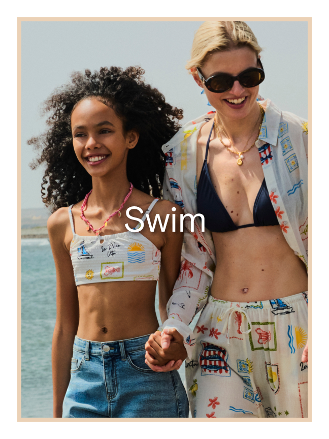 A woman and a girl near the sea wearing printed swimwear.
