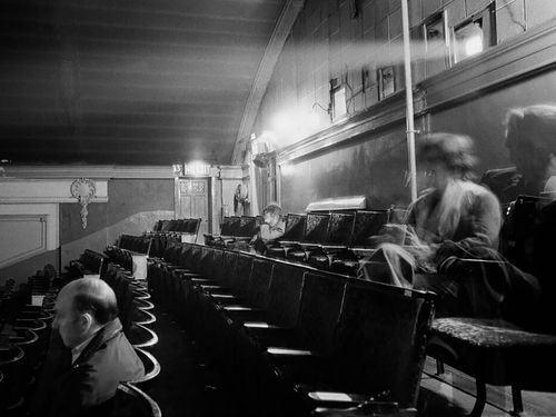 A number of figures sit in a movie theatre, with the light of a projector shining from behind them.