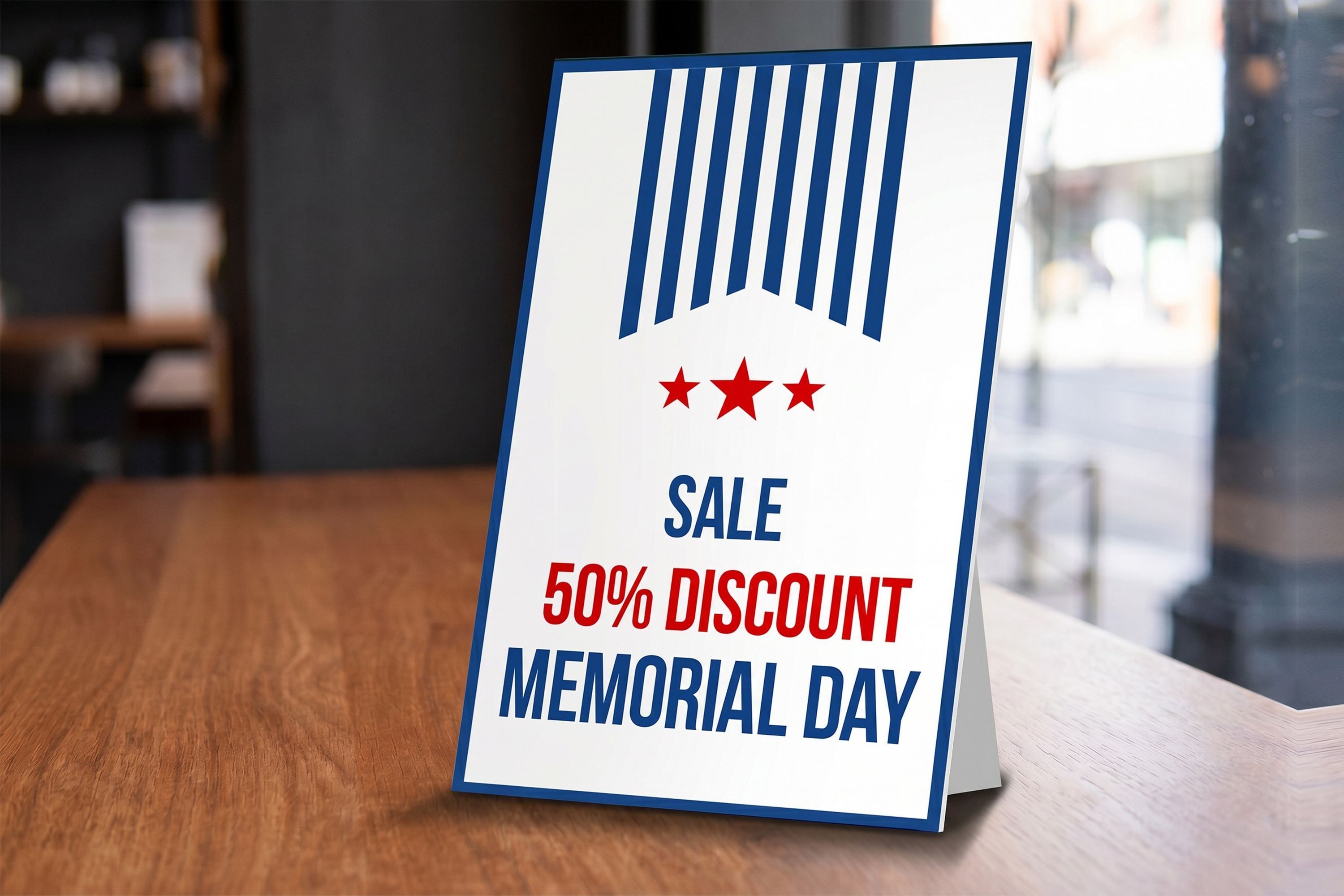 A tabletop counter card displays a Memorial Day sale promotion reading “SALE 50% DISCOUNT MEMORIAL DAY,” with red stars, blue vertical stripes, and red and blue text on a white background.