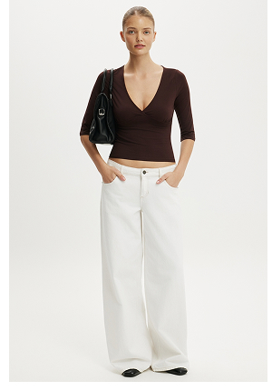 Woman wearing dark brown v-neck top with white wide-leg pants and black loafers