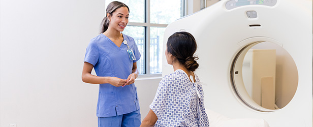Healthcare worker speaking with a patient seated beside a MRI scanner.