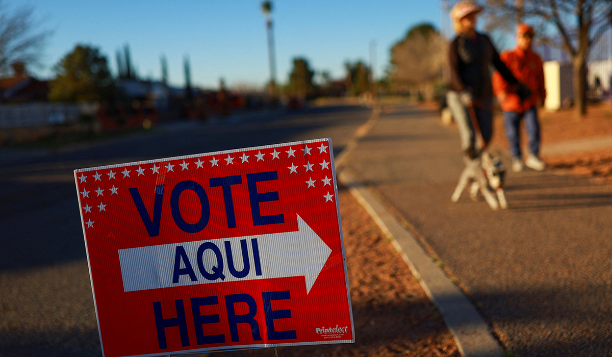 People walk a dog near a Vote Here sign.
