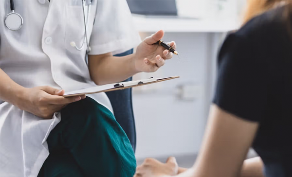  A doctor holding a clipboard and pen sits with a patient.
