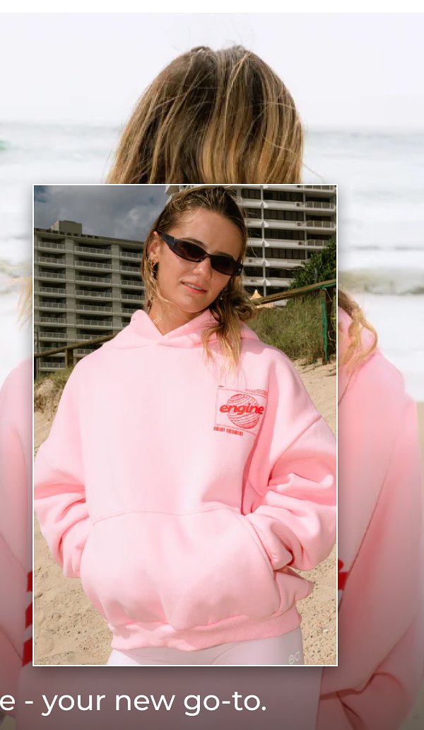 A person wearing a pink hoodie with sunglasses, standing outdoors near a building.