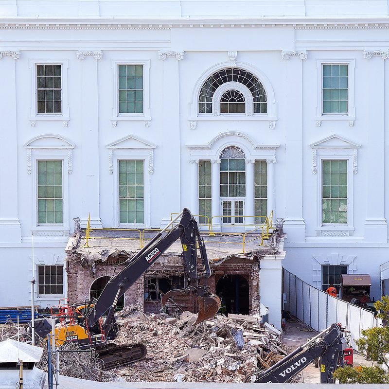 Heavy machinery breaks apart a building attached to the White House.