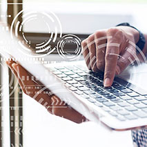 A hand types on a laptop keyboard while surrounded by electronic circles.