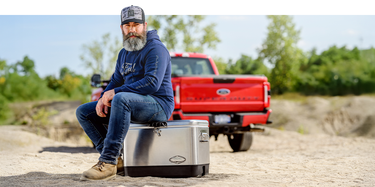 A person wearing Ford merchandise sits on a cooler in front of a parked Ford Super Duty&reg; truck