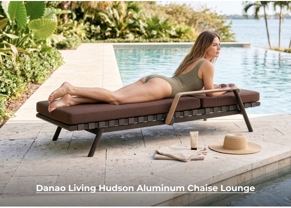 A woman in an olive green swimsuit lies on her stomach on a dark brown cushioned chaise lounge on a stone patio next to a swimming pool. Image Text: Danao Living Hudson Aluminum Chaise Lounge
