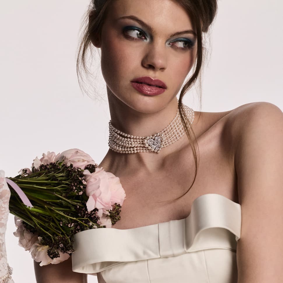 Image of model in a bridal gown, holding flowers, and wearing the material pearl heart choker necklace.