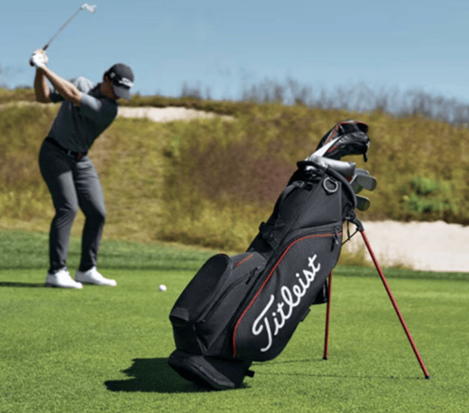 A Titleist golf bag and someone swinging on a golf ball in the background.