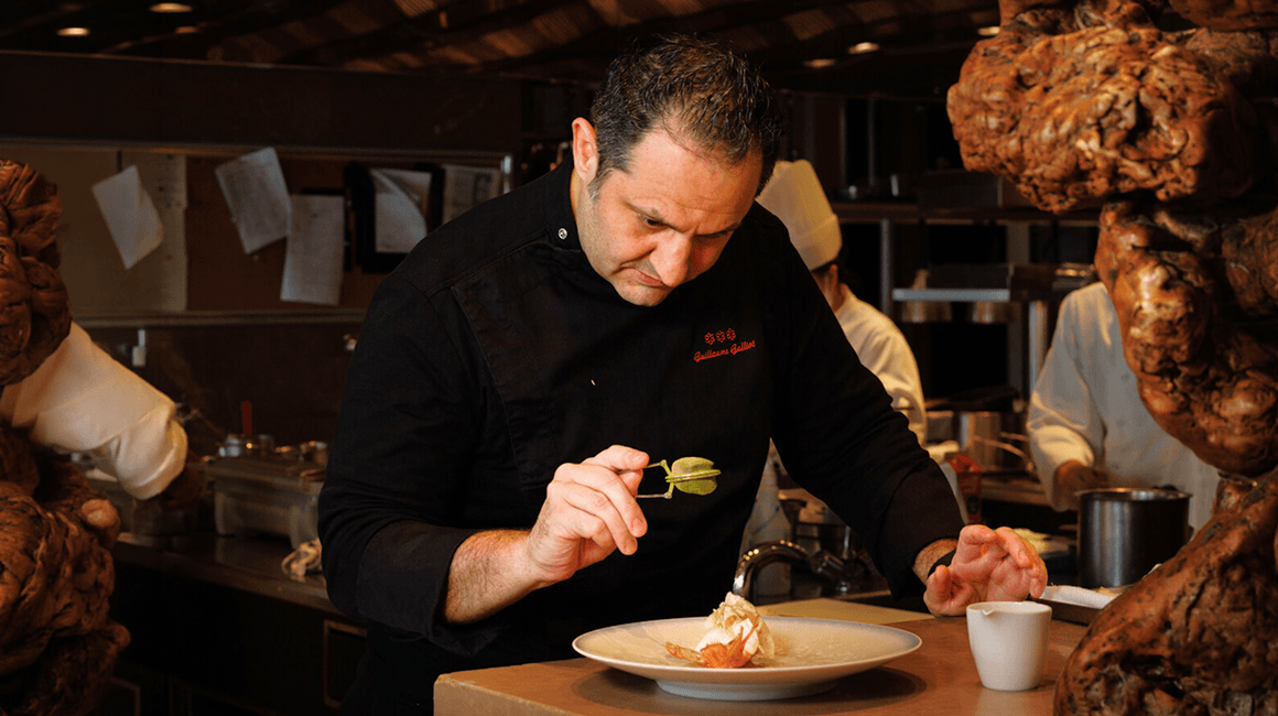 Chef carefully plating a fine-dining dish in a professional restaurant kitchen.