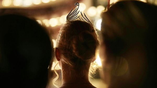 A woman wearing a swan shaped tiara watches young couples take part in the 68th edition of the Vienna Opera Ball