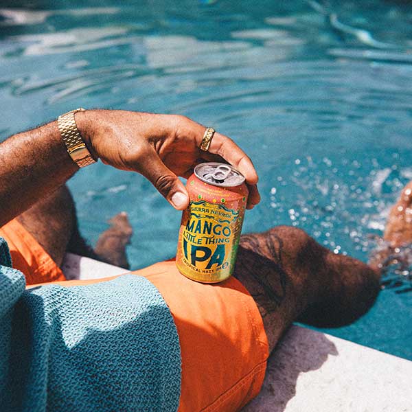 A young man holding a can of Mango Little Thing while dangling his legs into a pool