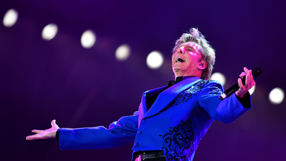 Barry Manilow is pictured on stage against a backdrop of lights.