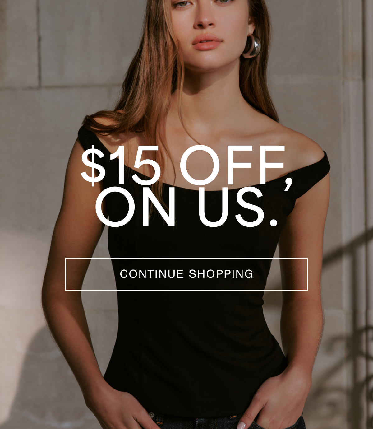 Bianca stands in soft sunlight wearing the black Eliana Top with an off-the-shoulder neckline, paired with dark jeans. Overlay text reads: “$15 OFF ON US,” with a “CONTINUE SHOPPING” button beneath.