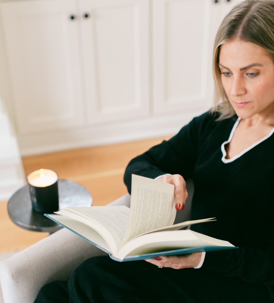 woman sitting and reading with lit candle next to her