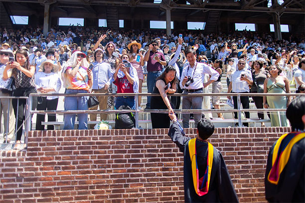 A graduating student holds his mother's hand in the Franklin Field stands at Commencement.