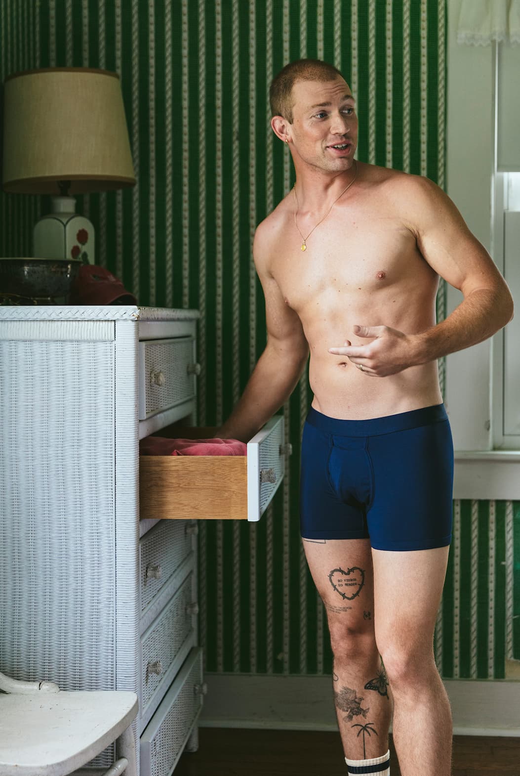 Shirtless man standing next to drawers wearing blue boxer briefs