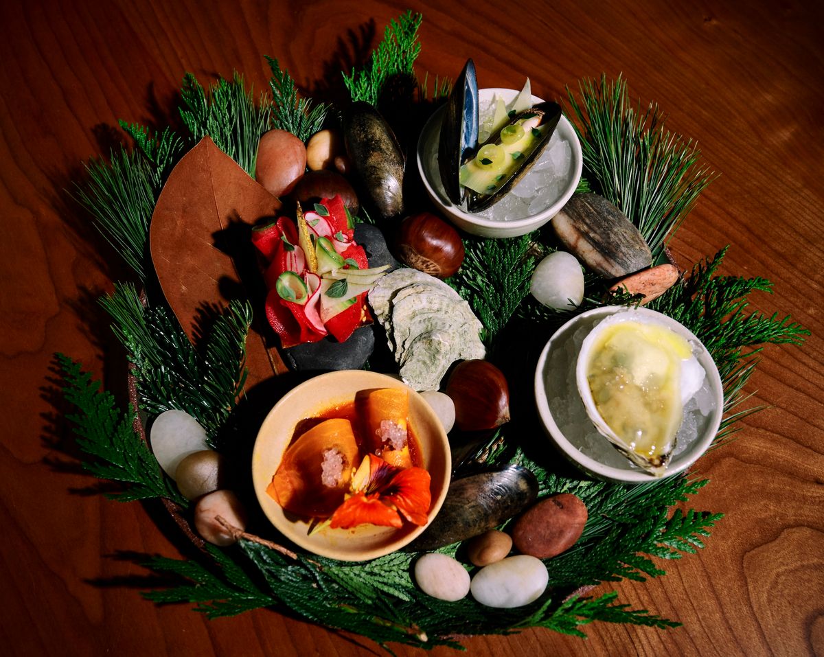 Small dishes of seafood displayed on a bed of pine branches and smooth stones.