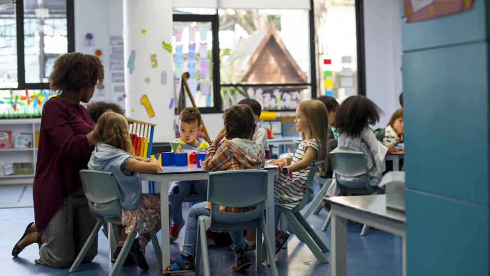 Image depicting a childcare provider or teacher with a group of children. Photo credit: Shutterstock.