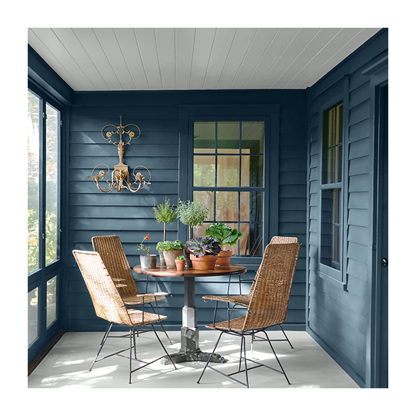 Enclosed blue-painted cabin porch with modern table, chairs, house plants, and wall light.
