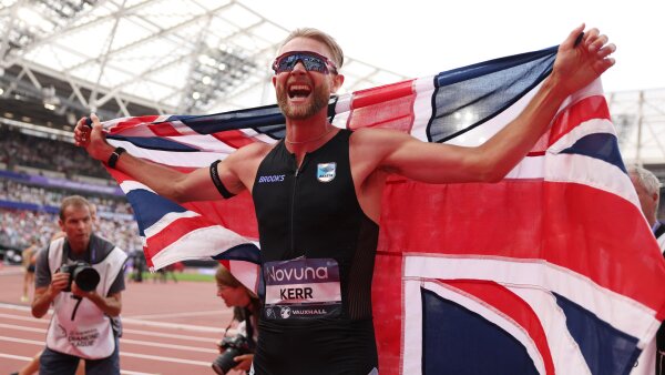 Josh Kerr of Team Great Britain celebrates after winning the 1 Mile Men's Final. He holds a British flag behind him. 