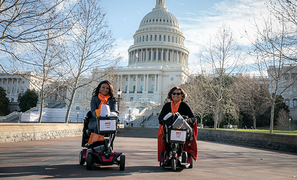 Two women sit on scooters in front of Capitol Hill    