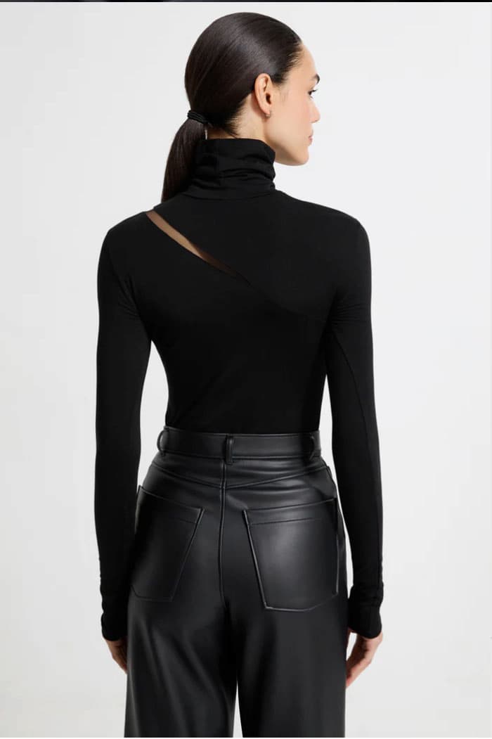 Back view of Mily in the black Vee turtleneck featuring an angled shoulder cutout, styled with high-waisted black leather pants.