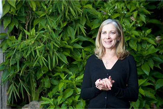 Profile photo of Dr. Jenny Gray arms clasped with a smile standing in front of a wall of plants. 