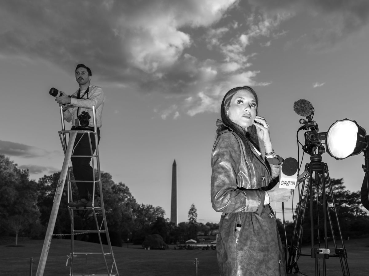 A woman holding a microphone is seen outdoors near camera equipment.