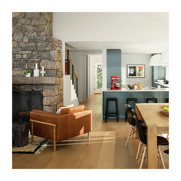 Open floor plan living space with stone hearth, leather seating, gray-blue kitchen counters, and a wooden dining table. 