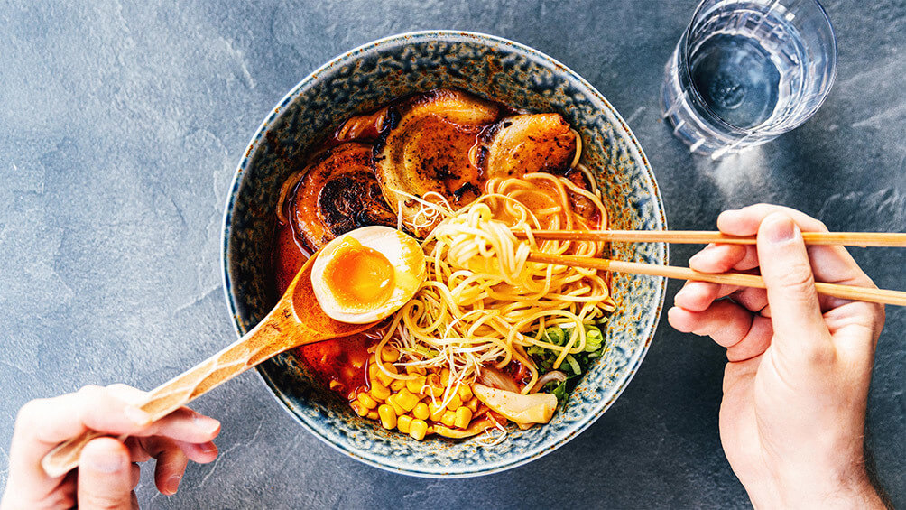 Image description: Overhead shot of person eating bowl of ramen at a restaurant.
