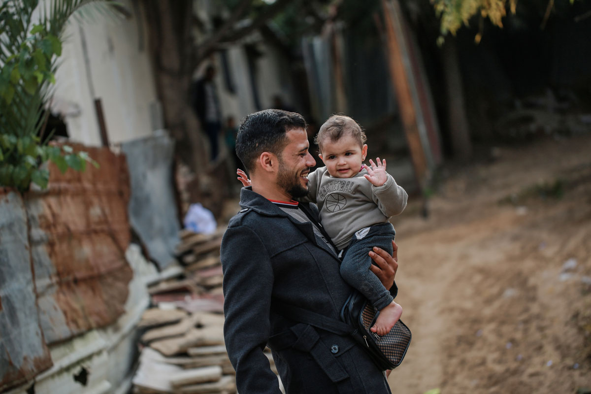 A man is carrying a small child while walking through an area with debris.