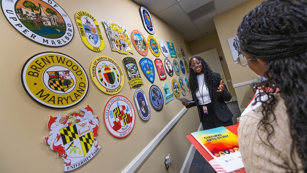 student intern holds papers in front of wall with seals from cities and towns in Prince George's County